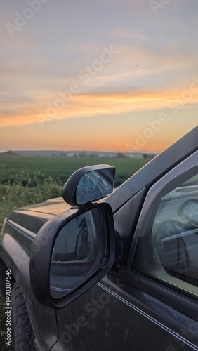Close-up of a jeep side mirror against a vivid orange sunset in nature