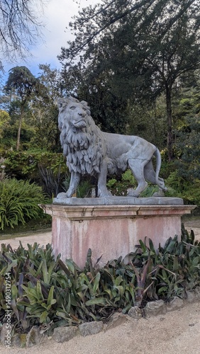 Majestic stone lion statue standing proud in public park surrounded by evergreen trees