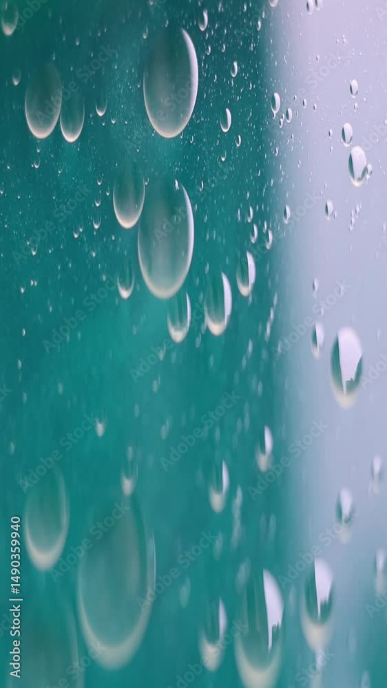 Una toma de cerca de varias burbujas de agua y aceite en movimiento en un fondo de color verde claro. Video vertical
