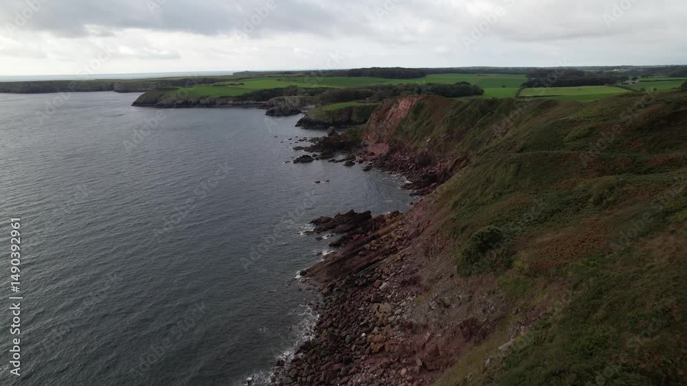 Rugged rocky sea coast on cloudy day. Forwards fly above seashore. Green pastures in background. South Wales, UK Rugged rocky sea coast on cloudy day. Forwards fly above seashore. Green pastures in background. South Wales, UK