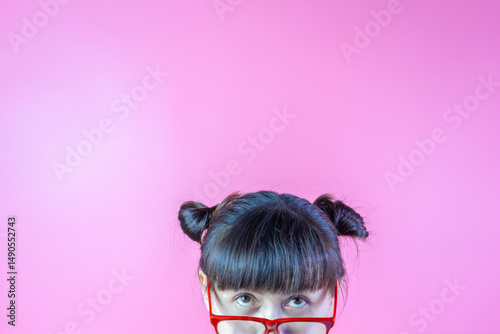 Funny lady hair two buns wearing red eyewear looking up isolated on pink background with copy space above head. Young woman cheerful in eyeglasses close up portrait headshot cropped face above lips.