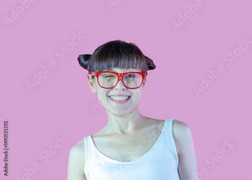Funny lady wearing red eyewear hair two buns winking cheeky smiling isolated on pink background with copy space. Close up portrait playful young woman in eyeglasses  for fun or secret.