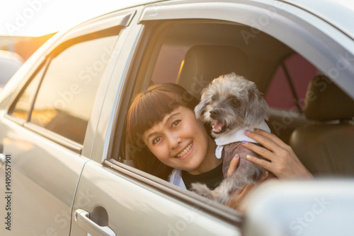 Young asian woman in casual outfit of cheerful with dog looking out of car window. Young female going on a road trip with her pet and smiling owner having good time together. Vacation with pet concept