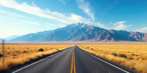 Asphalt ribbon unwinding towards a majestic, snow-capped mountain range under a vibrant, cloud-streaked sky, traversing a vast, golden expanse of desert grassland