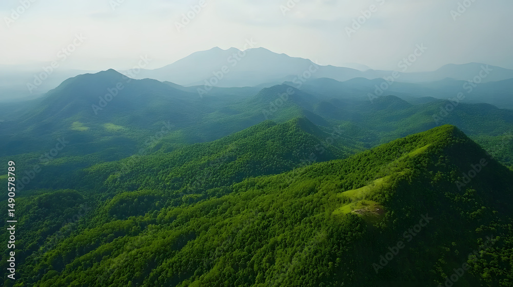 Naklejka premium Stunning aerial view of lush green mountains with rolling hills under a serene sky.