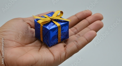A hand holding a small blue gift box tied with a golden ribbon bow top