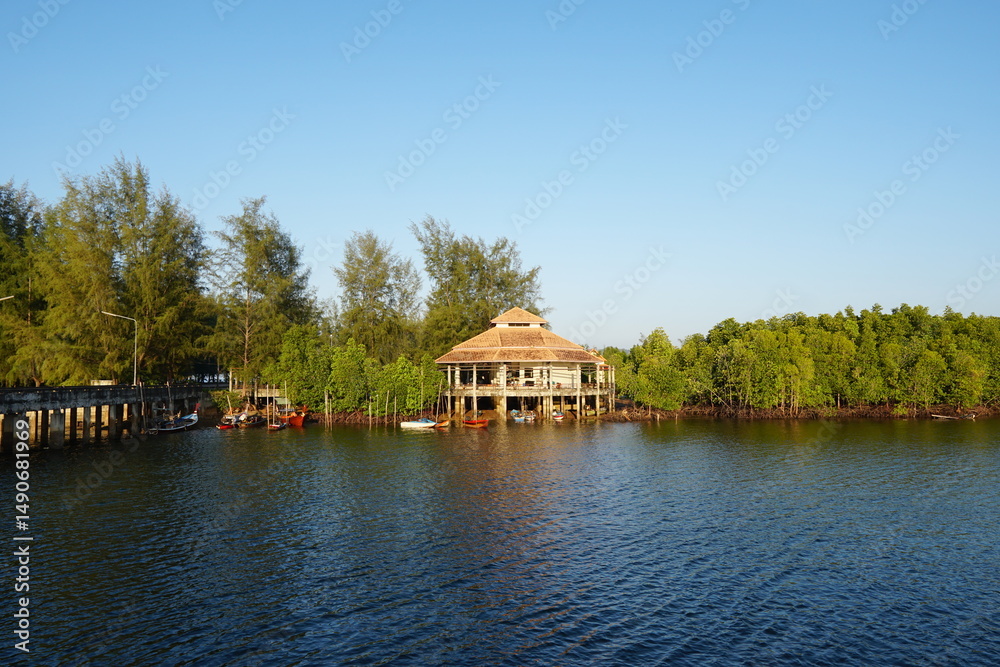 Obraz premium Peaceful waterfront house surrounded by lush greenery and calm water under clear blue sky
