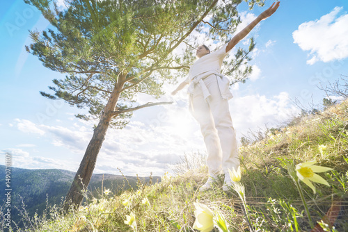 Arrival spring and summer. Joyful woman in white stands with her arms outstretched mountaint hill dotted with flowers and snowdrops. She welcomes the warmth of spring and spring. Wide-angle photo lens