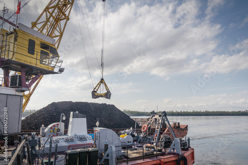 Large cranes are engaged in loading coal from a ship onto the dock. The port activity showcases a significant pile of coal, indicating active shipping operations.