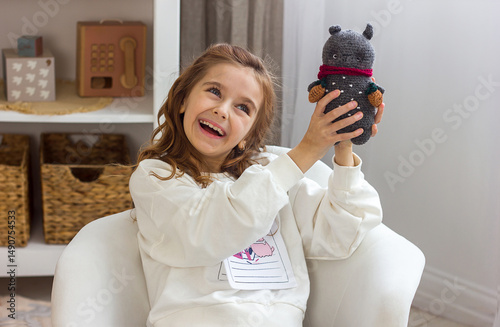 Beautiful little girl smiling holding soft knitted toy kigurumi on stylish children's room background, close-up portrait of handmade toy, selective focus