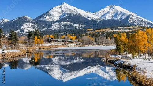 Stunning snow-capped peaks reflected in a serene lake, framed by golden autumn trees and a dusting of snow