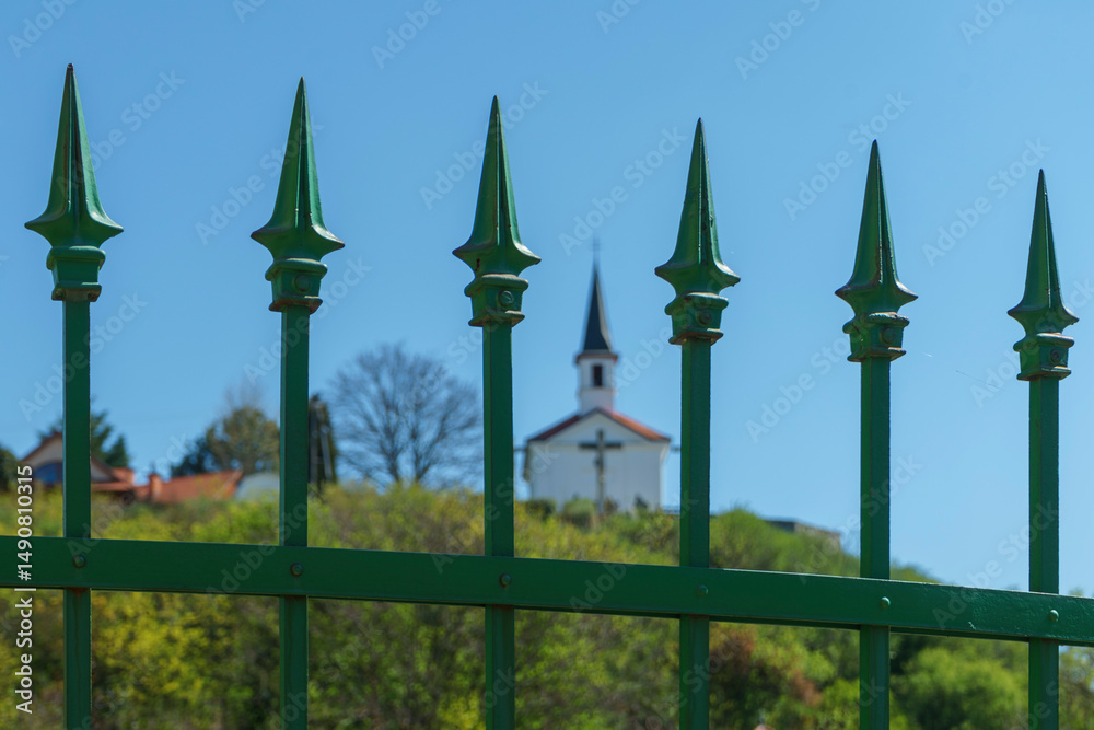 Fototapeta premium A small chapel on a distant mountain can be seen among the wrought iron fence pinnacles