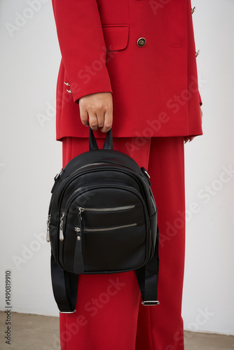 Stylish blonde woman poses with a trendy black backpack in a fashion studio setting