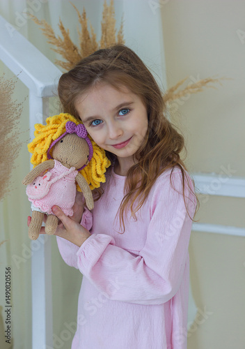 Beautiful little girl in pink dress smiling holding soft knitted toy kigurumi, close-up portrait, handmade toys, selective focus