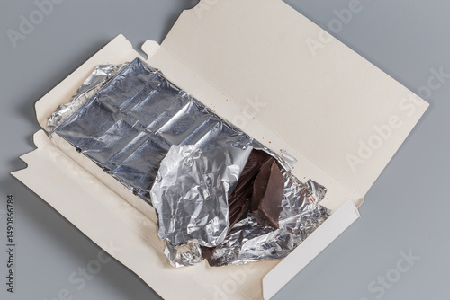 Partially broken off dark chocolate bar in open paper wrapper