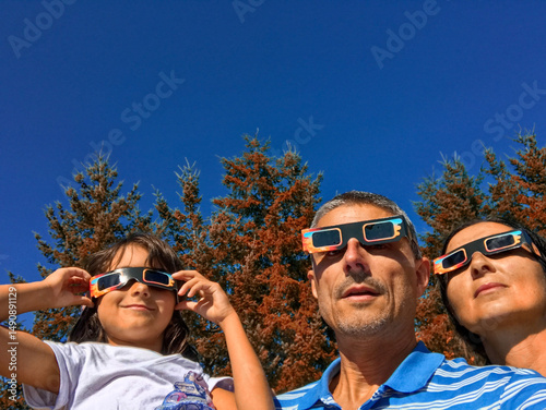 Excited family safely observing eclipse outdoors with special solar viewing glasses