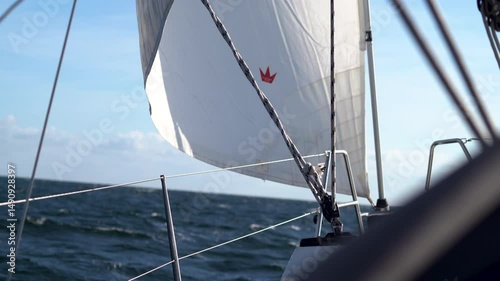 Sailboat at sea. The ocean appears choppy, with dark waves under a bright, mostly clear blue sky
