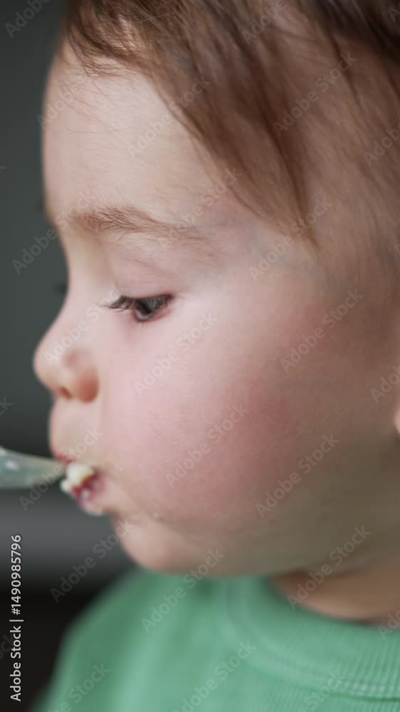 Feeding a little Caucasian baby with porridge from spoon. Mom's hand shoves the spoon to kid's face and he opens mouth obediently. Close up. Blurred backdrop. Vertical video Feeding a little Caucasian baby with porridge from spoon. Mom's hand shoves the spoon to kid's face and he opens mouth obediently. Close up. Blurred backdrop. Vertical video