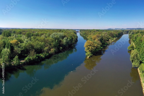 Die Lechmündung in die Donau zeigt eine friedliche Flusslandschaft mit üppiger Vegetation und klarem Wasser. Die Spiegelung der Bäume im Wasser und der blaue Himmel schaffen eine idyllische Atmosphäre