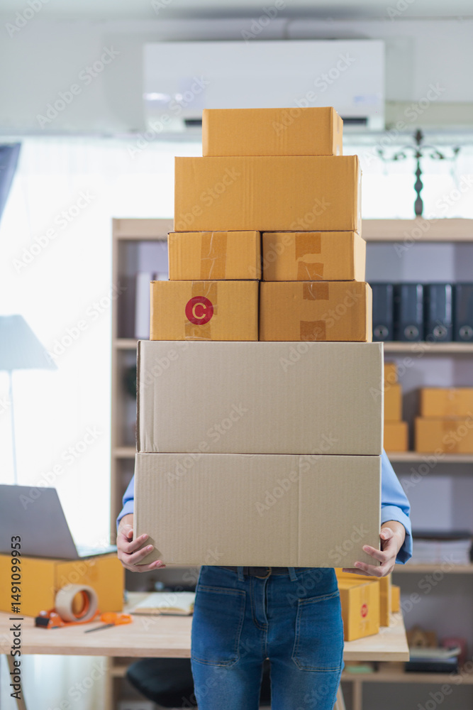 Fototapeta premium A young businesswoman who started her small SME business is lifting a large number of parcel boxes to be delivered to a shipping company to deliver the products to customers who have ordered them.
