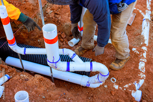 Construction workers lay down sewage drainage pipes in trench ensuring proper installation for water flow.