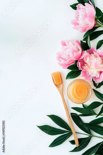 Golden sugaring paste in glass jar with wooden spatula, pink peonies and green leaves, spa beauty concept, white background