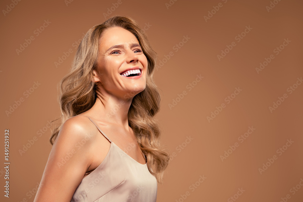 Fototapeta premium Smiling mature woman with beautiful blonde hair and elegant beige outfit, exuding confidence and vitality