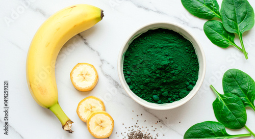 Spirulina powder with banana and spinach on marble background