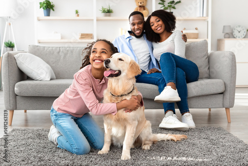 Wallpaper Mural Man's Best Friend. Portrait of smiling black girl hugging her happy dog in living room at home, looking away, cheerful parents sitting on the couch and looking at daughter playing with pet Torontodigital.ca