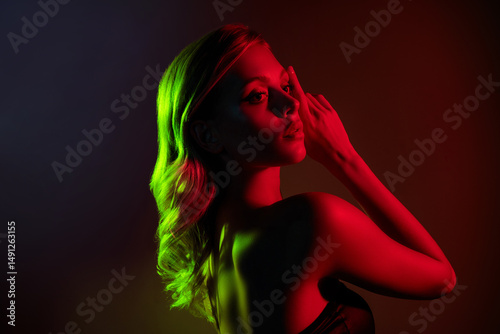 Glamorous young woman with blond hair and naked shoulders in neon red and green lighting on dark background photo