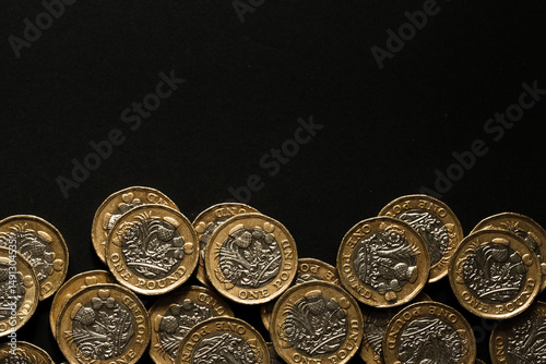 Scattered British one pound coins lined along the bottom of a black background, symbolising savings, wealth, and UK currency, Stafford, United Kingdom, May 18, 2025..