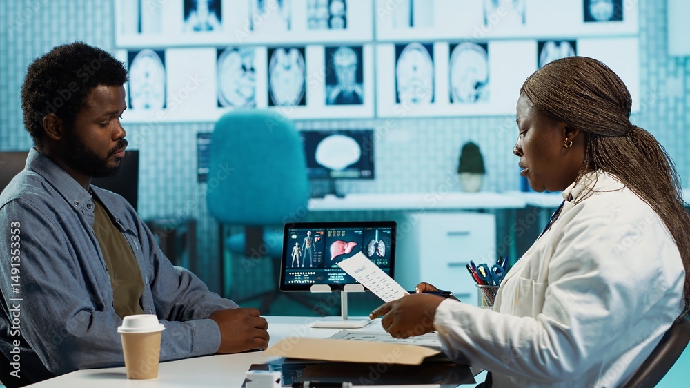 Female physician using radiology scans and reports to advise patient during checkup focusing on diagnosis and treatment. African american doctor with medical expertise consults casual man. Camera A. Female physician using radiology scans and reports to advise patient during checkup focusing on diagnosis and treatment. African american doctor with medical expertise consults casual man. Camera A.