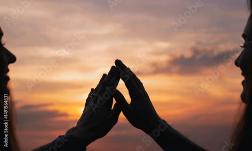 Silhouetted hands forming a triangle against a vibrant sunset sky, symbolizing connection and unity