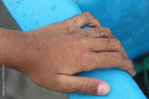 Close-up of a child's sandy hand gripping a blue boat part. This photo captures the textures and colors of seaside activity, childhood curiosity, and outdoor adventure
