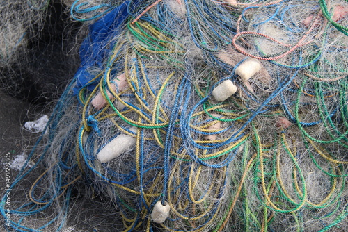 Close-up of tangled colorful fishing nets with various ropes and buoys. The intricate texture and mix of lines in green, blue, pink, and yellow create a chaotic yet visually engaging composition, repr