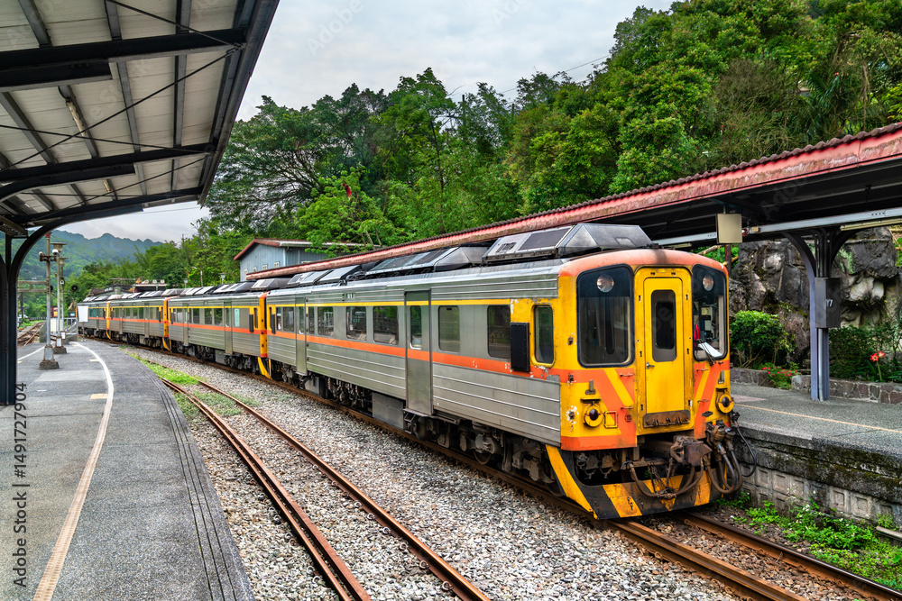 Fototapeta premium Local passenger train waits at the platform of Shifen Station, nestled in the lush green hills of New Taipei, Taiwan. The scenic station is part of the historic Pingxi Line, popular with tourists for