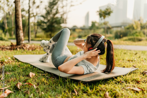 A woman dressed in workout clothes is wearing headphones and listening to music while exercising her abdominal muscles.