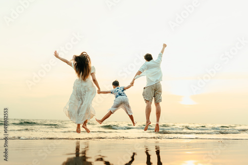 Family jumping happily with their hands raised, having fun on the beach with family during a holiday, travel, long weekend, summer or any other holiday. They are happy to spend time together.