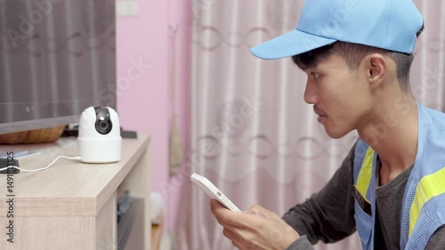 asian male technician installs and sets up wireless security cameras using smartphone at customer's home