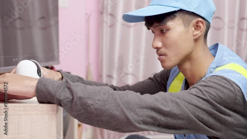 asian male technician installs and sets up wireless security cameras using smartphone at customer's home