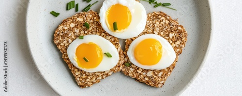Three poached eggs on multigrain toast garnished with chives, served on a light gray plate.