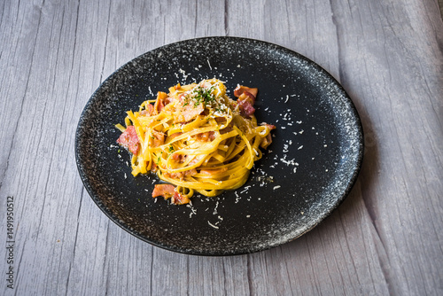 Carbonara with ham cream and cheese served on a black plate