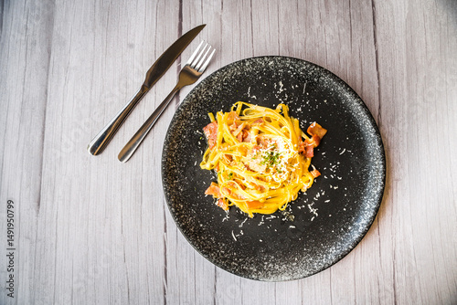 Carbonara with ham cream and cheese served on a black plate