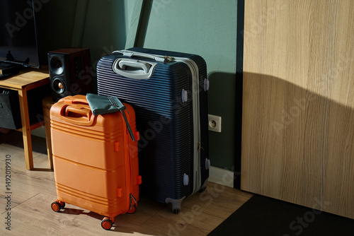 Fotografie Two modern suitcases, orange and navy, stand near entrance door in morning light