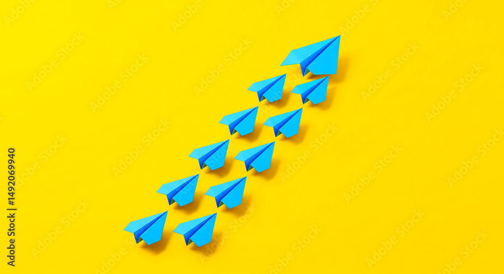 Fototapeta premium A group of blue paper airplanes flying upwards on a bright yellow background in a diagonal arrangement