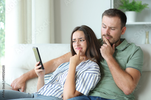 Suspicious couple checking phone content sitting in a couch