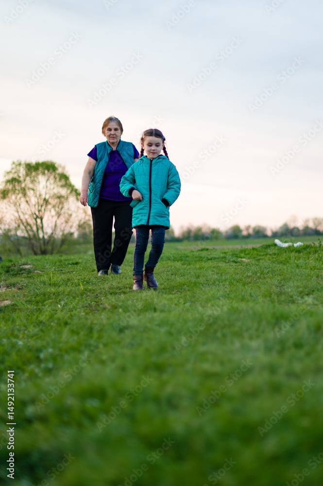 Grandmother and granddaughter enjoying a walk in a green field. A heartwarming moment of family bonding in nature. Grandmother and granddaughter enjoying a walk in a green field. A heartwarming moment of family bonding in nature.