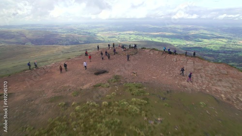 People admiring lookout from mountain summit. Backwards fly above distinctive peak in landscape. Brecon Beacons national Park, Wales, UK