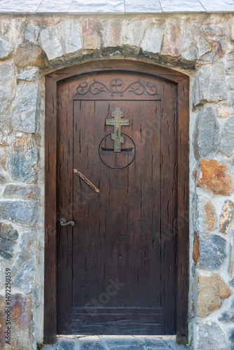 Old Wooden door with cross emblem stone wall entrance. Rustic door surrounded by rock wall with christian cross design.