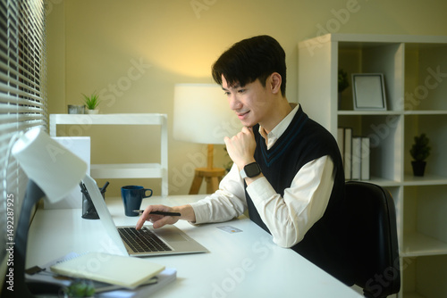 Young entrepreneur in a sweater vest uses a laptop at a minimalist desk photo